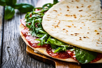 Italian piada wraps - piadina stuffed with fresh vegetable leaves and salami sausage on wooden table
