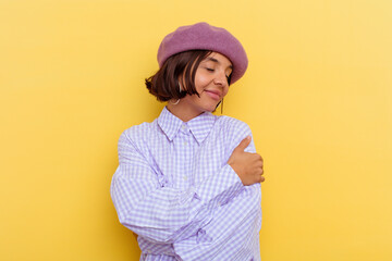 Young mixed race woman wearing a beret isolated on yellow background hugs, smiling carefree and...