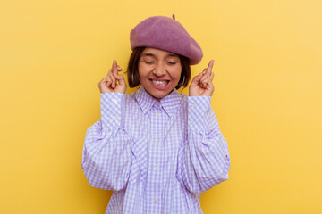 Young mixed race woman wearing a beret isolated on yellow background crossing fingers for having luck