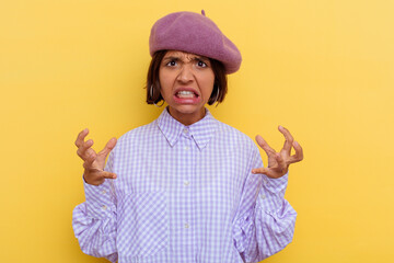 Young mixed race woman wearing a beret isolated on yellow background screaming with rage.