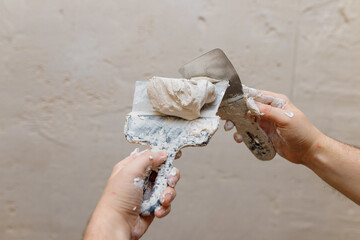 Male hands with spatula using putty for wall, builder making overhaul.