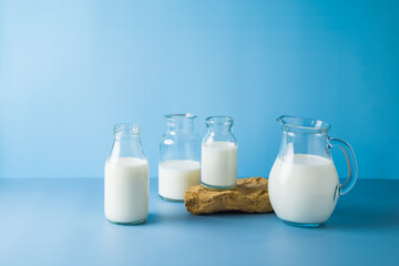 Milk bottles and milk jug over blue background. Modern still life composition. Healthy eating concept