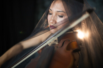 An Asian young woman is playing violin. Violinist is performing on the stage with the veil on her....
