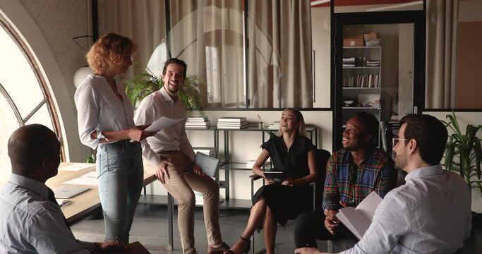 Happy young female team leader holding negotiations meeting with mixed race employees, presenting research result, discussing project issues or developing new ideas, sitting in circle in boardroom.