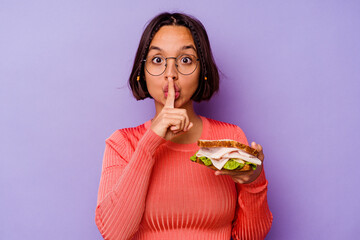 Young mixed race woman holding a sandwich isolated on purple background keeping a secret or asking...