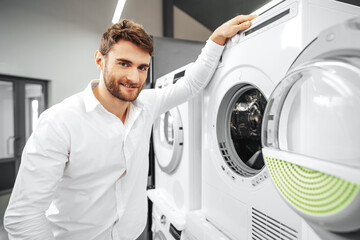 Young man choosing new washing machine in household appliances store