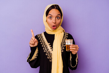 Young Moroccan woman holding a glass of tea isolated on purple background having some great idea, concept of creativity.