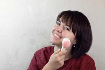 Young pretty woman doing facial massage with a brush. Close-up portrait, anti-aging facial massage at home, daily morning routine. 