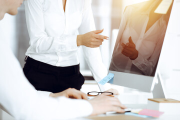 Unknown businessman and woman discussing questions while using computer and blocknote in sunny office, close-up. Teamwork in business