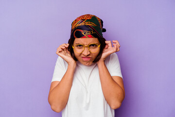 Young mixed race woman wearing a bandana isolated on purple background covering ears with hands.