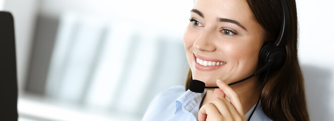 Brunette female customer service representative in a headset is consulting clients online. Call...