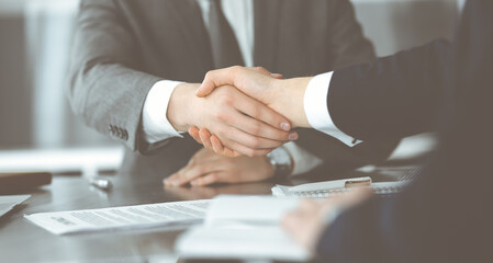 Unknown businessman shaking hands with his colleague or partner above the glass desk in modern office, close-up. Business people group at meeting