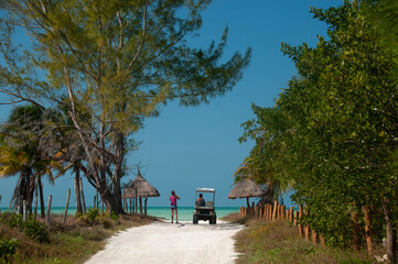 Rear view of a young tourist couple driving a golf cart into the white sandy tropical beach on the island of Holbox in Mexico. Concept travel tourism