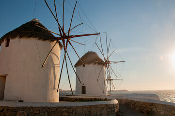 The old windmills on the island of Mykonos at sunset in Greece. In the background the coast and the Aegean sea.