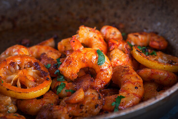 Shrimps fried in a pan with lemon and garlic on a dark rustic background. Top view.