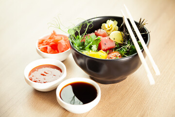 Poke salad with tuna in a bowl. Ingredients fresh tuna, cherry tomatoes, marinated seaweed, rice, takuan, Ponzu sauce, Teriyaki sauce, nori, sesame seeds, lime, cilantro. Asian seafood salad concept.