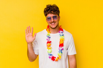 Young caucasian man wearing a Hawaiian party stuff isolated on yellow background smiling cheerful...