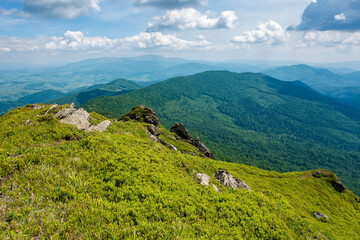view from pikui mountain. huge stones on the grassy slopes. summer landscape of carpathian mountains. borzhava ridge in the distancee beneath a sky with clouds