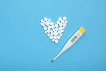 heart shaped from white pills and thermometer on blue background, copy space concept of cardiology and therapy