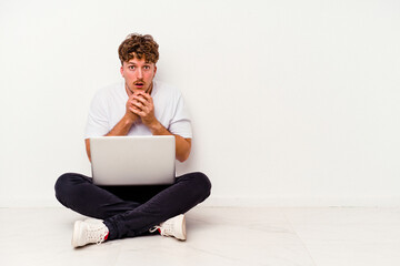 Young caucasian man sitting on the floor holding on laptop isolated on white background scared and afraid.