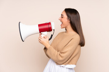 Young caucasian woman isolated on beige background shouting through a megaphone