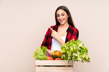 Farmer with freshly picked vegetables in a box isolated on beige background pointing finger to the side