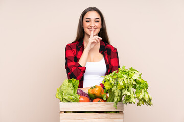 Farmer with freshly picked vegetables in a box isolated on beige background doing silence gesture