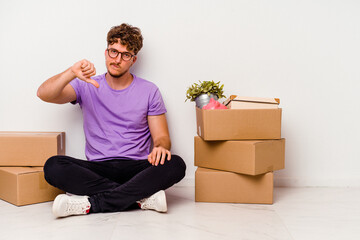 Young caucasian man sitting on the floor ready for moving isolated on white background showing a...