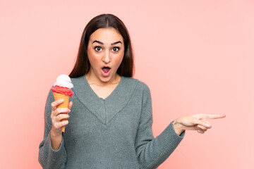 Young woman holding a cornet ice cream isolated on pink background surprised and pointing side