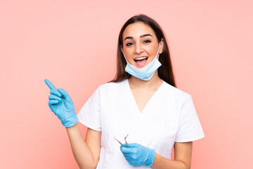 Woman dentist holding tools isolated on pink background pointing finger to the side