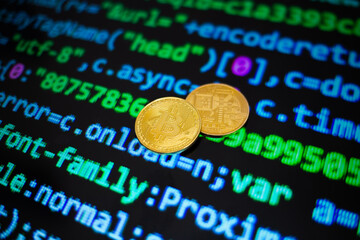 Two gold bitcoin coins on the background of lines of program code