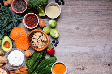 Healthy food ingredients. Above view side border on a wooden background. Copy space. Super food concept with green vegetables, berries, whole grains, seeds, spices and nutritious items.