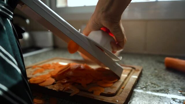 Person On The Kitchen Slicing Carrots By Manual Grater Slicer. - Close Up Shot