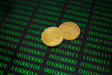 Two gold coins bitcoin on the background of green zeros and ones of the program code