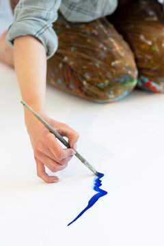 Painting Art. Creative Hobby. Talent Inspiration. Female Artist Hand Drawing Blue Abstract Portrait Face Outline Silhouette With Paintbrush On White Paper Sitting On Floor.