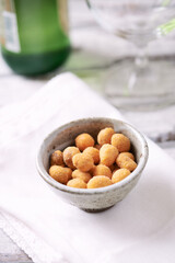 Spicy nuts in a ceramic dish; a bottle of beer in background. Bright wooden background. Close up.