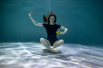 beautiful girl in a black swimsuit meditates underwater with a bright lotus flower on a blue background 
