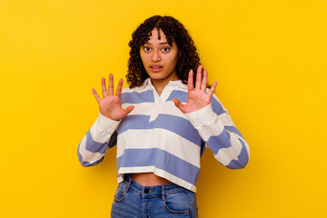 Young mixed race woman isolated on yellow background rejecting someone showing a gesture of disgust.