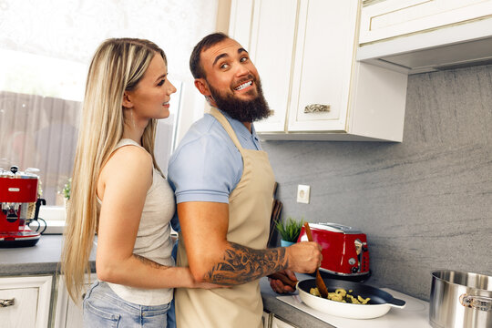Young man and woman cooking food in kitchen together, happy couple preparing food