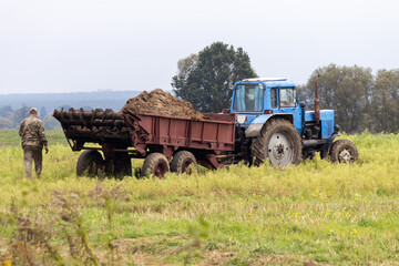 A farmer uses a tractor to spread manure on the field for a better harvest.
