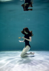 a beautiful girl in a black swimsuit underwater holds an aquarium with fish in her hands and admires them 