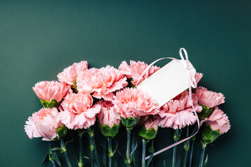 Bouquet of pink carnations with blank tag on dark green background.
