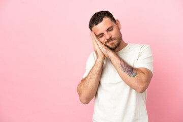 Young Brazilian man isolated on pink background making sleep gesture in dorable expression