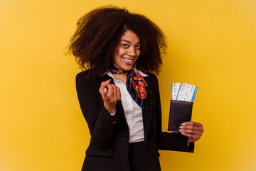 Young african american air hostess holding a plane tickets isolated on yellow background  pointing...