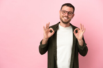 Young Brazilian man isolated on pink background showing ok sign with two hands