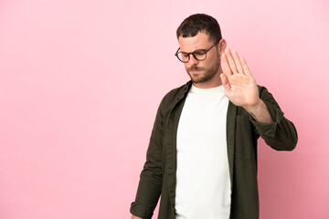 Young Brazilian man isolated on pink background making stop gesture and disappointed