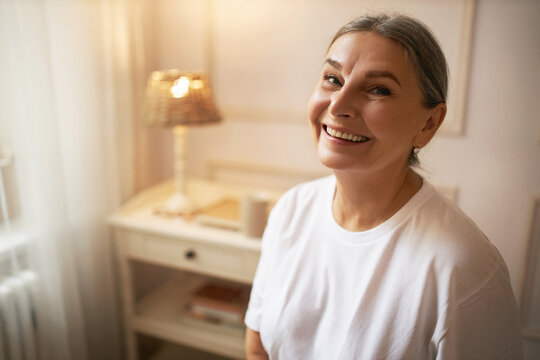 Positive human emotions, joy and happiness. Indoor image of attractive mature European woman relaxing at home, having happy carefree facial expression, smiling broadly, showing straight healthy teeth
