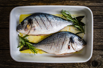 Fresh dorada and herbs in cooking pot on wooden background
