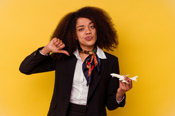 Young african american air hostess holding a little plane isolated on yellow background showing a...