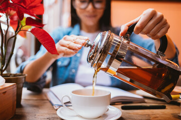 Young woman student with glasses pours tea into cup